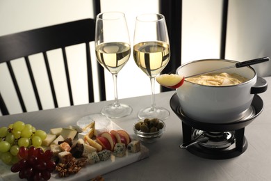 Photo of Fork with piece of apple, melted cheese in fondue pot, wine and products on grey table