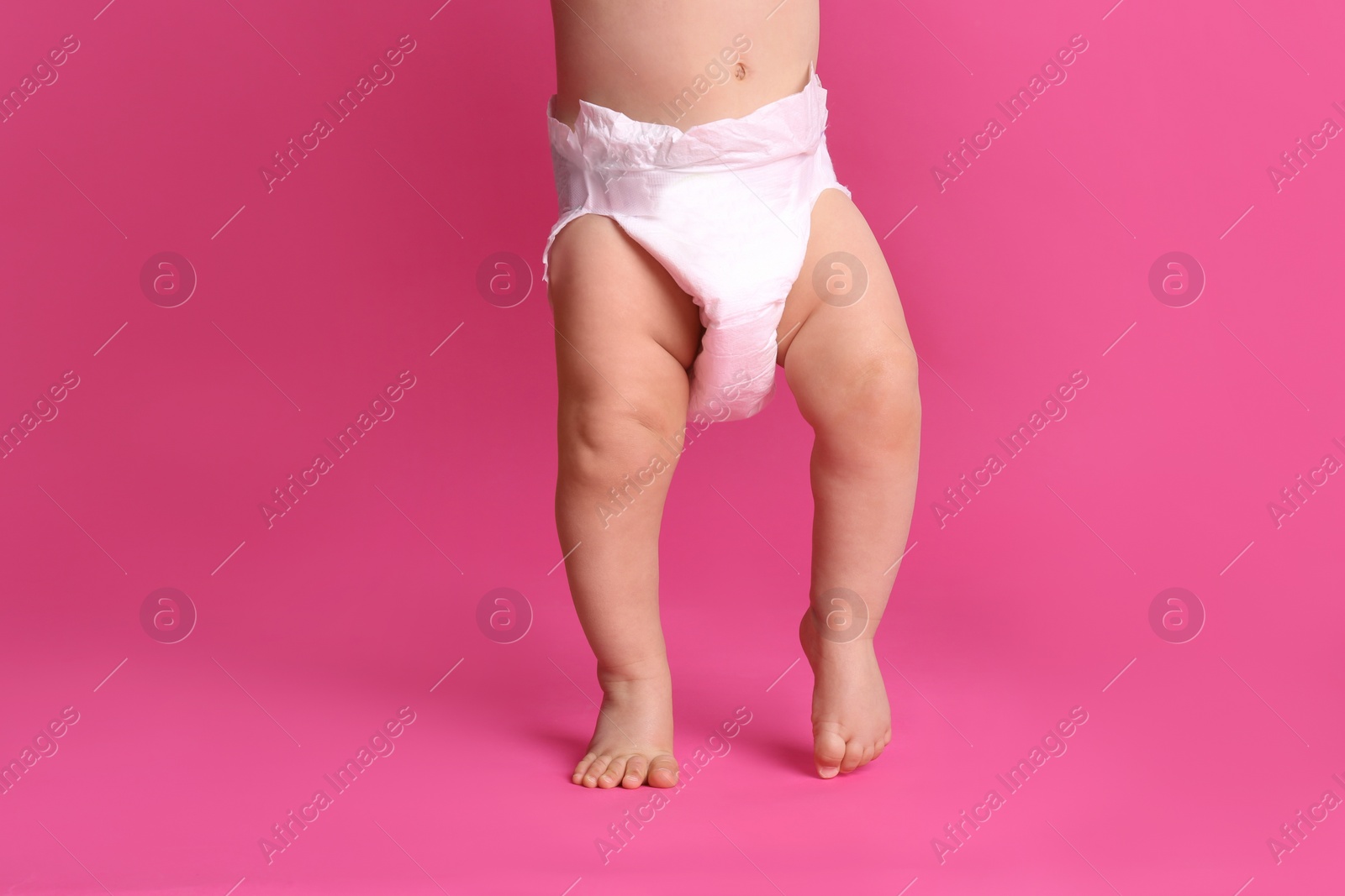 Photo of Cute baby in dry soft diaper standing on pink background, closeup