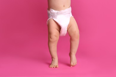 Photo of Cute baby in dry soft diaper standing on pink background, closeup