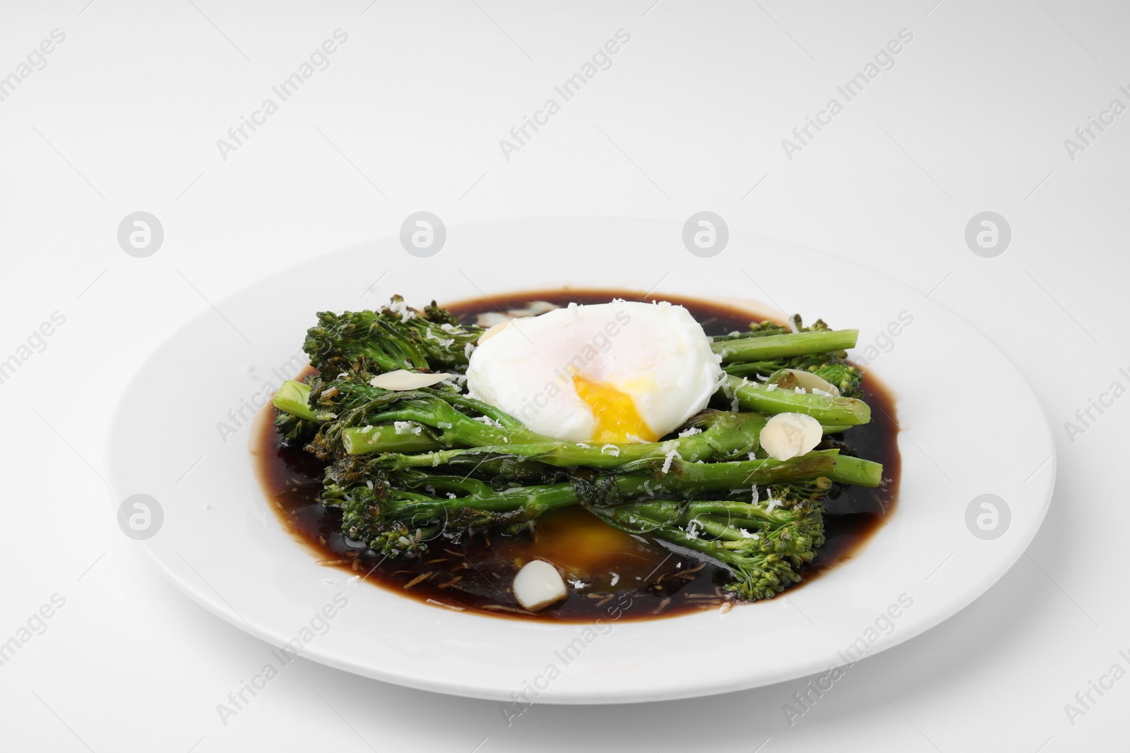 Photo of Tasty cooked broccolini with poached egg, almonds and sauce on white background, closeup