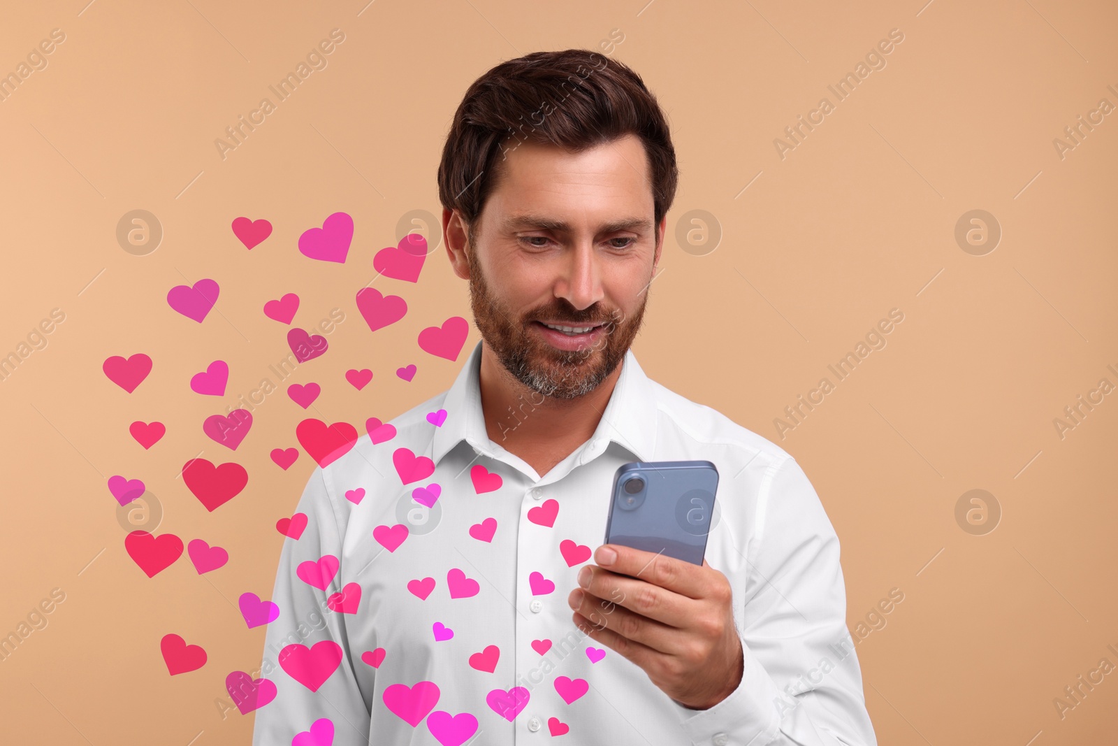 Image of Long distance love. Man chatting with sweetheart via smartphone on dark beige background. Hearts flying out of device
