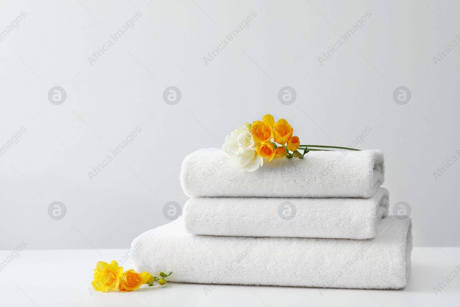 Photo of Stack of fresh towels with flowers on table against white background. Space for text