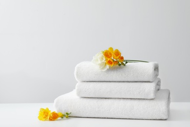 Stack of fresh towels with flowers on table against white background. Space for text