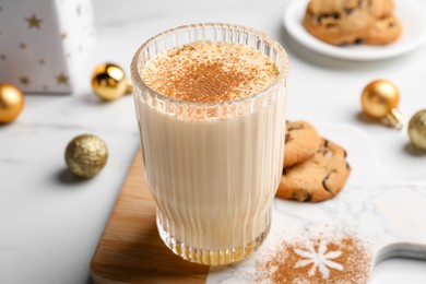Photo of Glass of delicious eggnog with cinnamon on white table, closeup