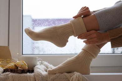 Photo of Woman in warm socks sitting near window at home, closeup