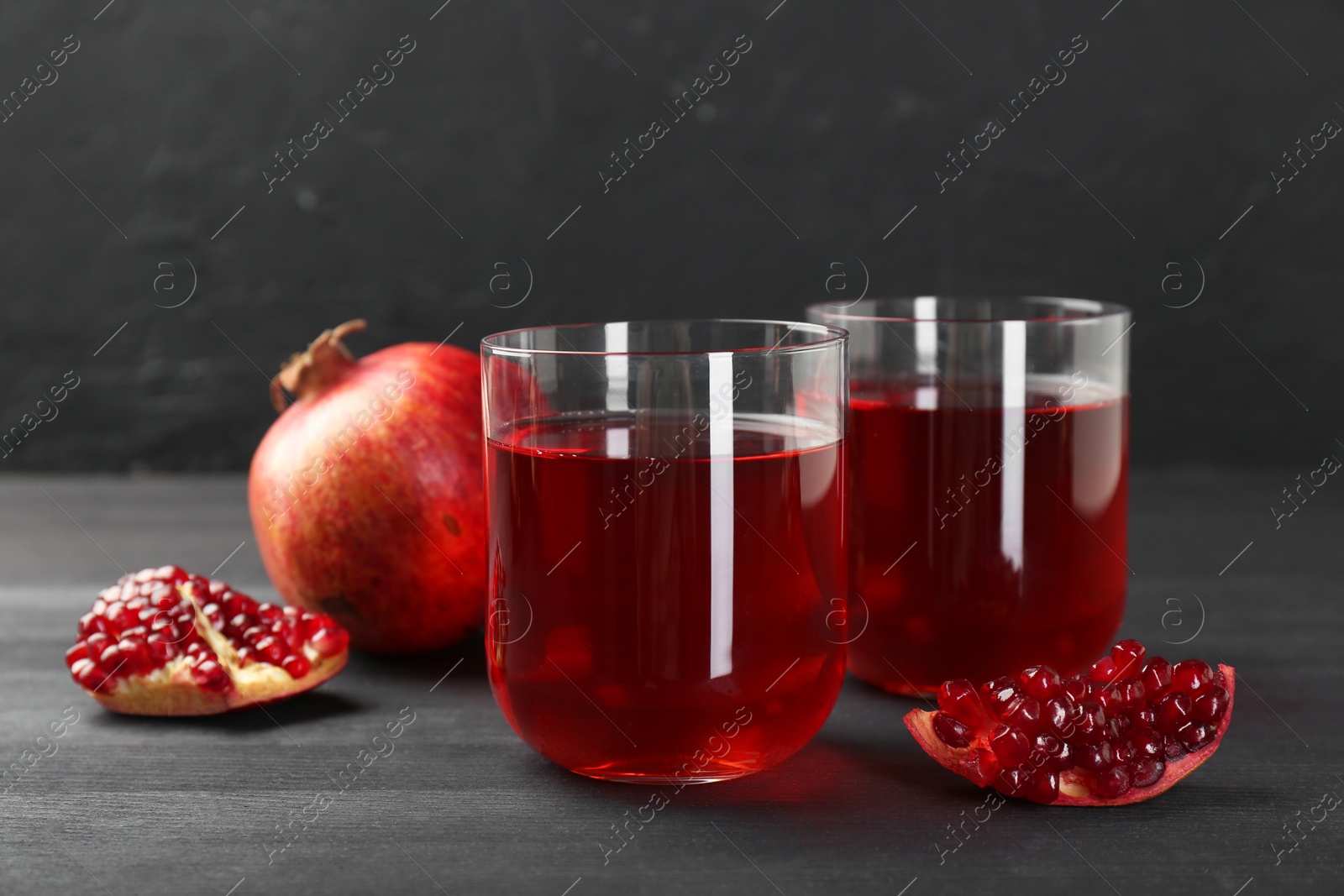 Photo of Tasty pomegranate juice in glasses and fresh fruits on black wooden table