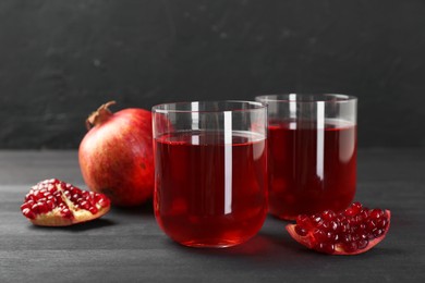 Photo of Tasty pomegranate juice in glasses and fresh fruits on black wooden table