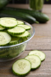 Photo of Cut cucumber in glass bowl on wooden table, closeup