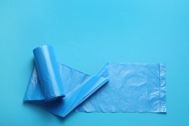 Photo of Roll of turquoise garbage bags on light blue background, top view. Space for text