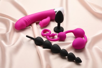 Photo of Pink and black sex toys on beige silky fabric