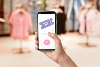 Woman holding smartphone with activated promo code in clothes store, closeup