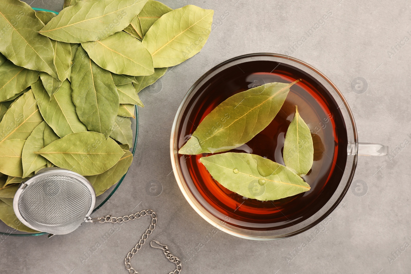 Photo of Cup of freshly brewed tea with bay leaves on grey table, flat lay