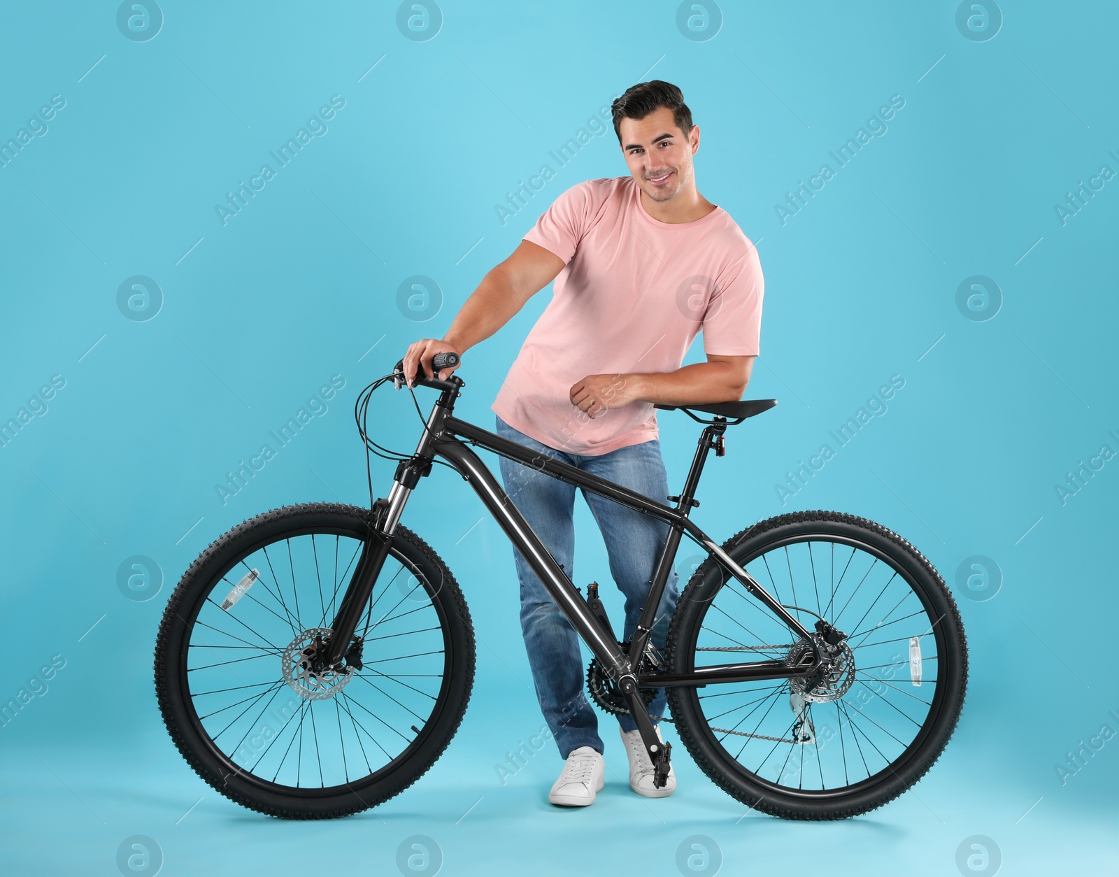 Photo of Handsome young man with modern bicycle on light blue background