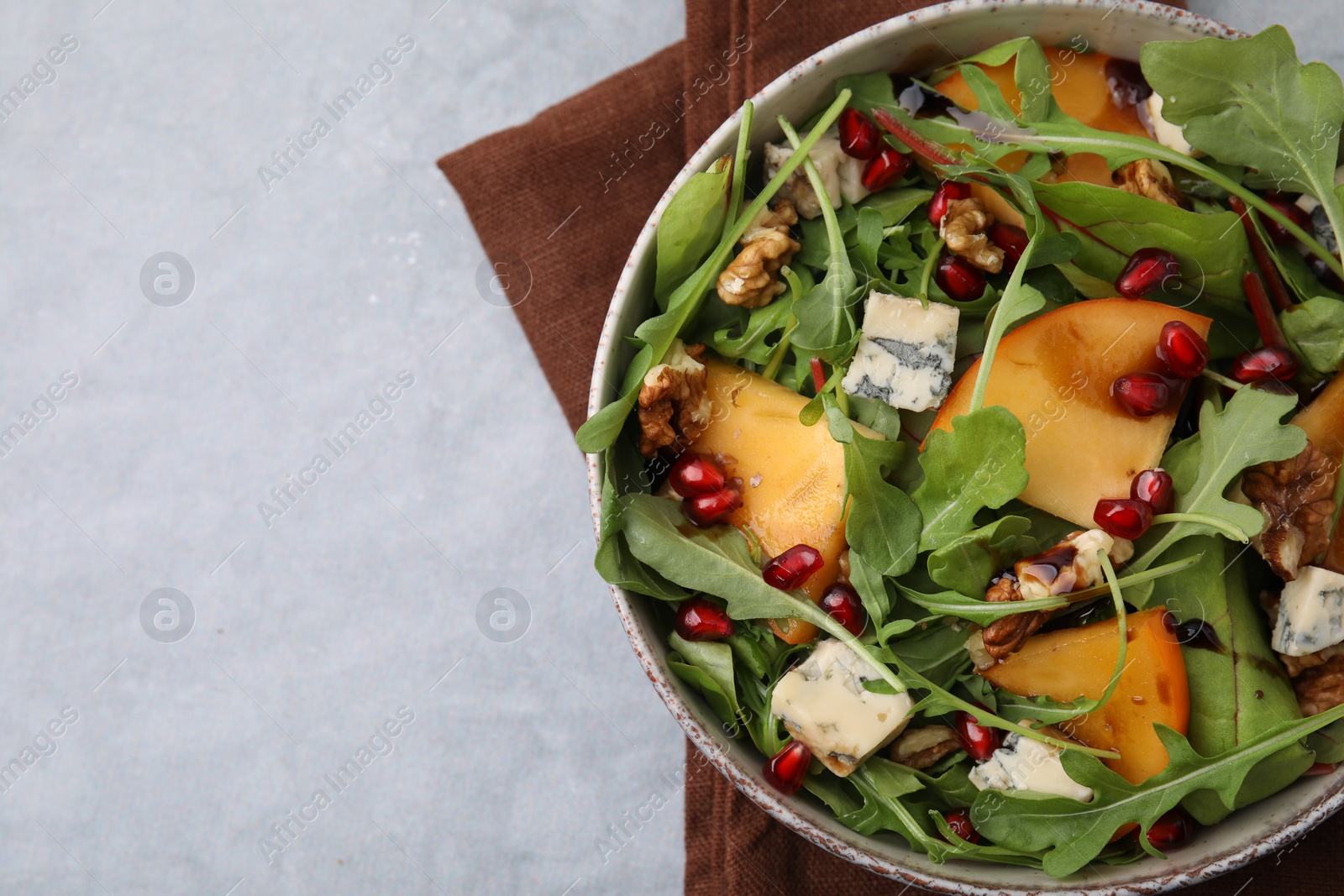 Photo of Tasty salad with persimmon, blue cheese, pomegranate and walnuts served on light grey table, top view. Space for text