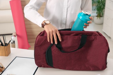 Businesswoman packing sports stuff for training into bag in office, closeup 