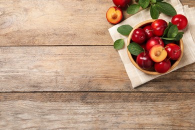 Photo of Delicious ripe cherry plums with leaves on wooden table, flat lay. Space for text
