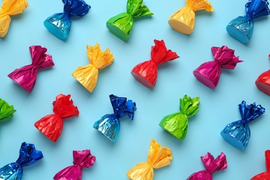 Photo of Candies in colorful wrappers on light blue background, flat lay