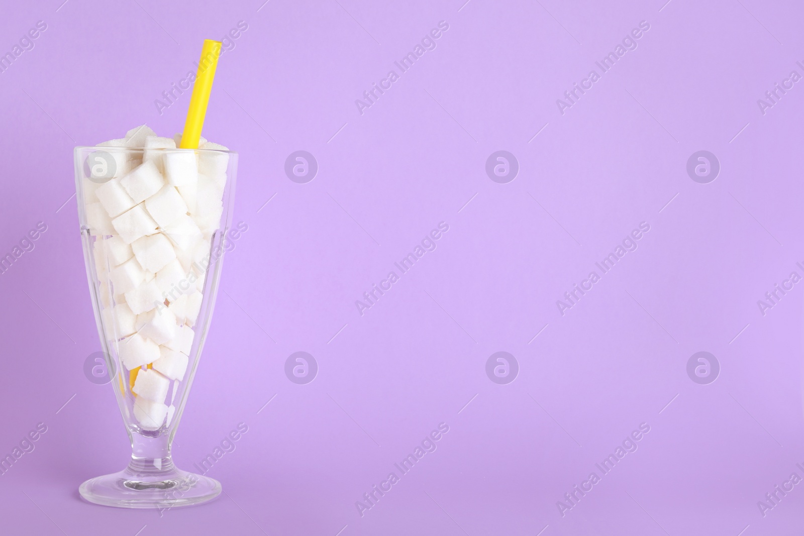 Photo of Refined sugar cubes in cocktail glass with straw on lilac background. Space for text