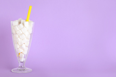 Photo of Refined sugar cubes in cocktail glass with straw on lilac background. Space for text