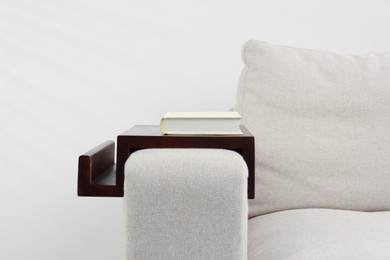 Photo of Book on sofa with wooden armrest table indoors. Interior element