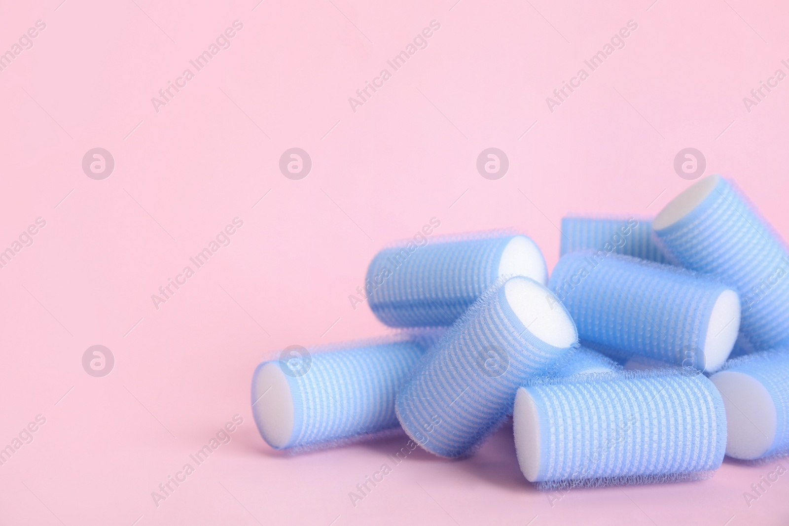 Photo of Many light blue hair curlers on pink background, space for text
