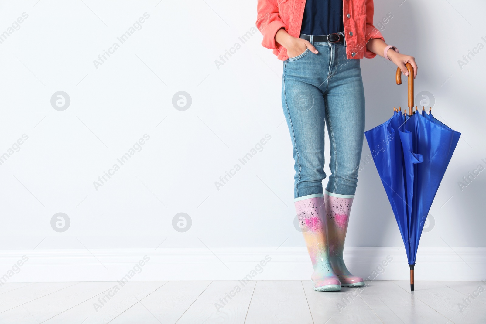 Photo of Woman in gumboots holding bright umbrella near white wall with space for design