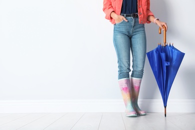 Woman in gumboots holding bright umbrella near white wall with space for design