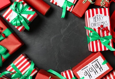 Photo of Frame of Christmas gift boxes with green bows on dark grey background, flat lay. Space for text