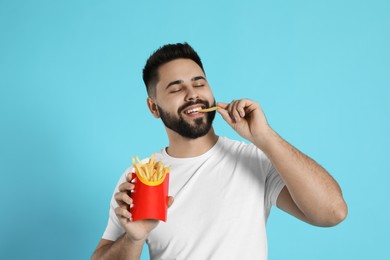 Young man eating French fries on light blue background