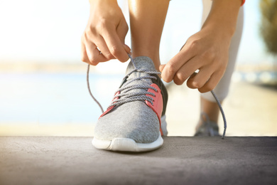 Image of Sporty woman tying shoelaces outdoors on sunny day, closeup