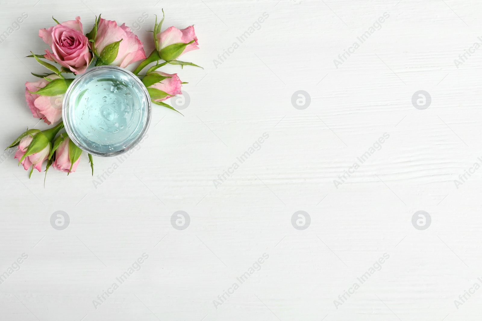 Photo of Flat lay composition with cosmetic gel and beautiful flowers on white wooden table. Space for text