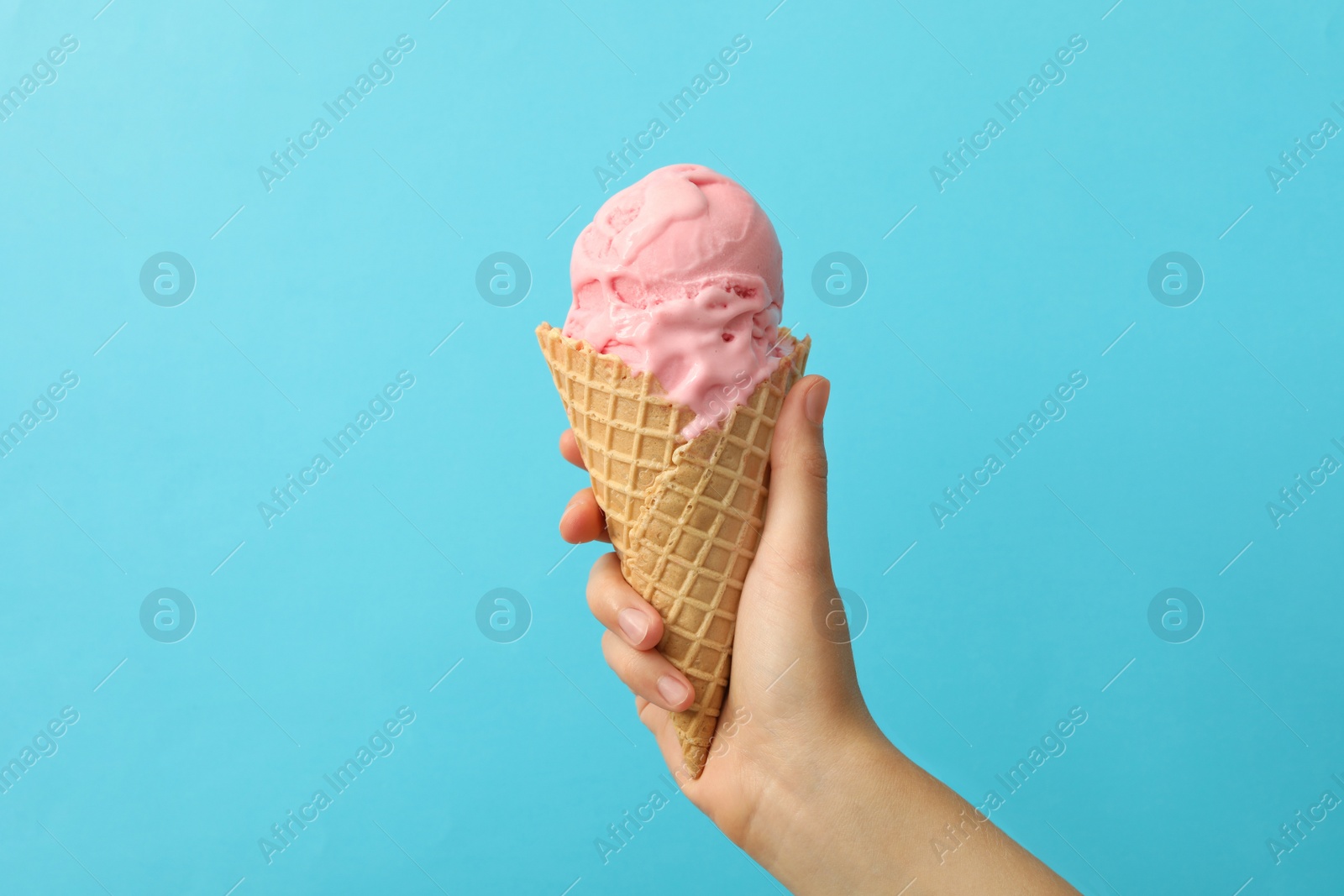 Photo of Woman holding waffle cone with delicious pink ice cream on light blue background, closeup