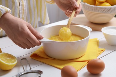 Photo of Woman cooking lemon curd at white wooden table, closeup