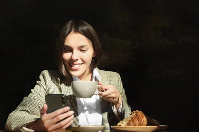 Special Promotion. Happy young woman with cup of drink using smartphone at table in cafe