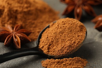 Photo of Spoon with cinnamon powder and star anise on grey table, closeup