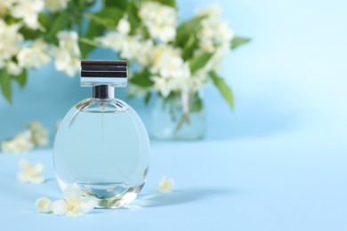 Aromatic perfume in bottle and beautiful jasmine flowers on light blue background, closeup. Space for text