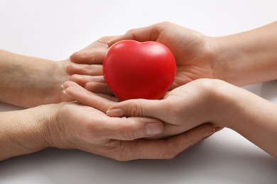 Young and elderly women holding red heart on white background, closeup