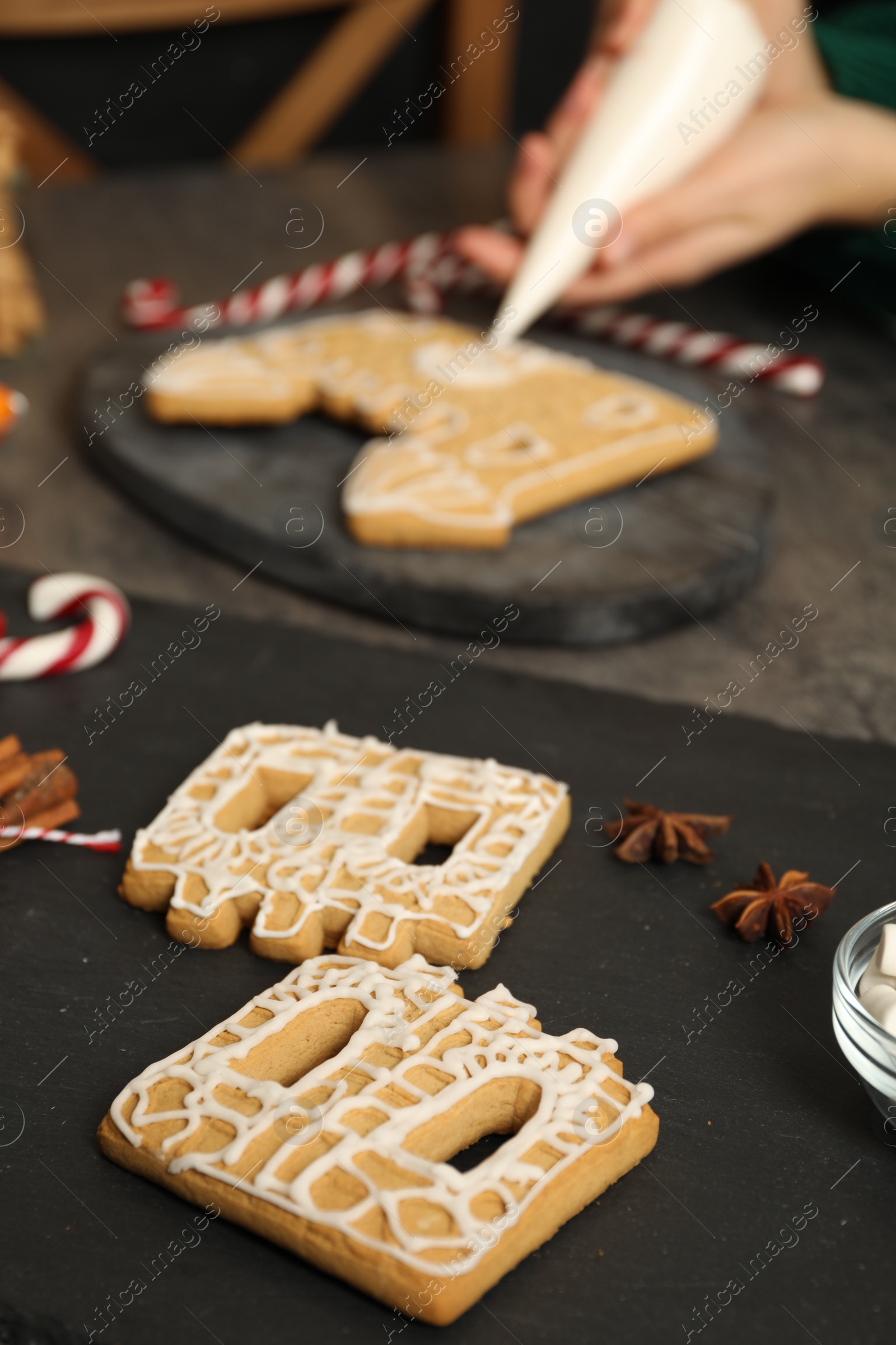 Photo of Woman decorating gingerbread house with icing at grey table, focus on parts