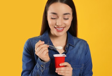 Photo of Happy woman with tasty yogurt on orange background