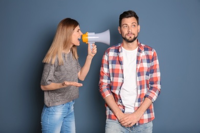 Young woman with megaphone shouting at man on color background