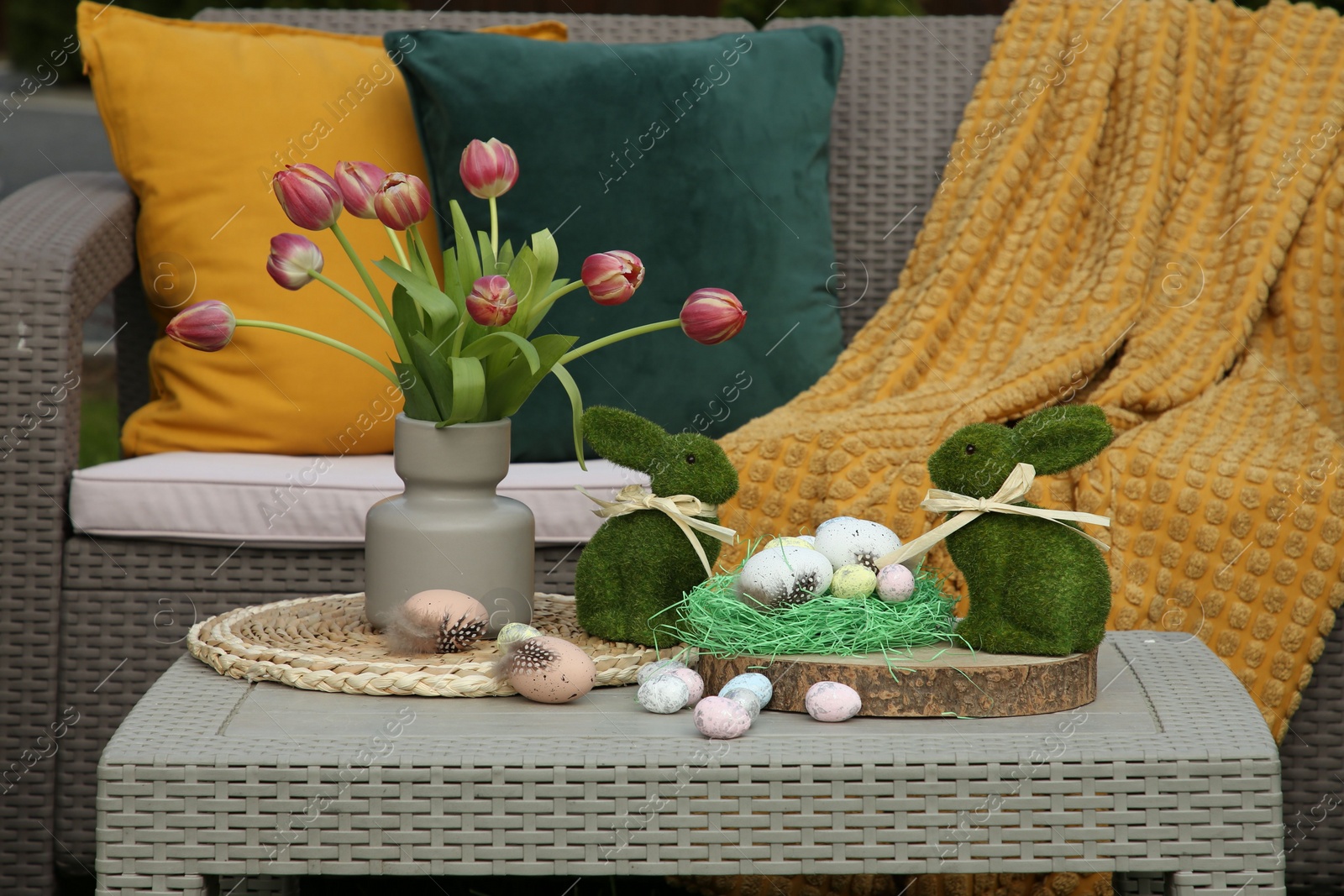 Photo of Terrace with Easter decorations. Bouquet of tulips in vase, bunny figures and decorated eggs on table outdoors