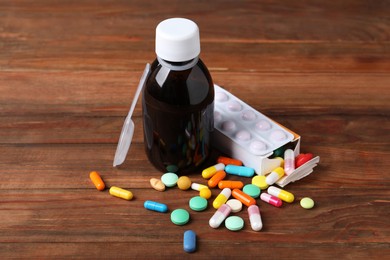Photo of Bottle of syrup, dosing spoon and pills on wooden table. Cold medicine