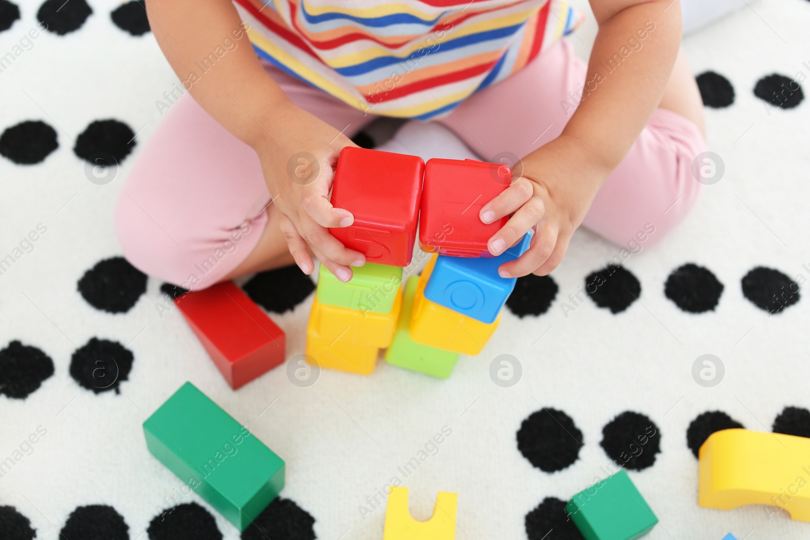 Photo of Cute little girl playing with colorful cubes on floor indoors, above view. Educational toy