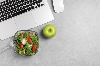 Photo of Fresh vegetable salad, apple, fork and laptop on light grey table at workplace, flat lay. Business lunch