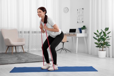 Photo of Happy woman doing morning exercise with stretching band at home. Space for text