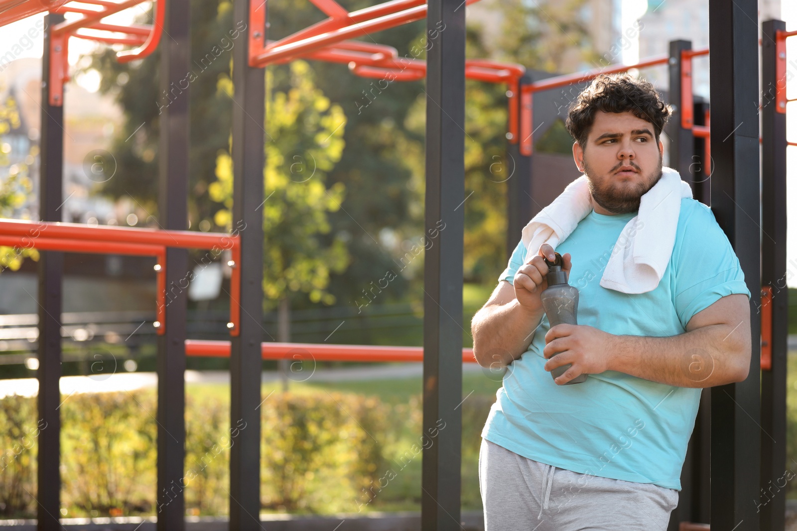 Photo of Young overweight man with bottle and towel on sports ground