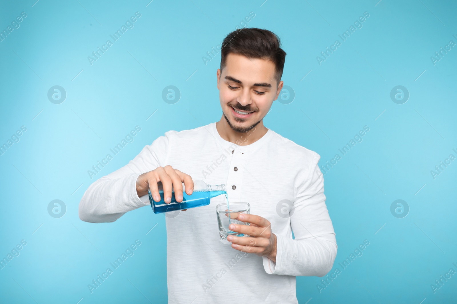 Photo of Young man pouring mouthwash from bottle into glass on color background. Teeth and oral care