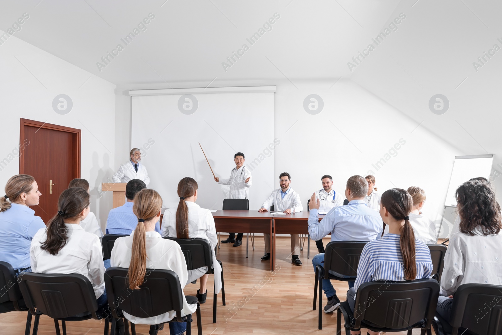 Photo of Doctors giving lecture near projection screen in conference room