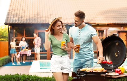 Photo of Young man and woman with drinks near barbecue grill outdoors