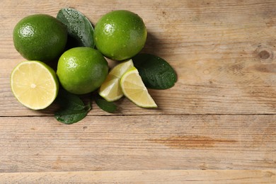 Photo of Fresh ripe limes and green leaves with water drops on wooden table, flat lay. Space for text